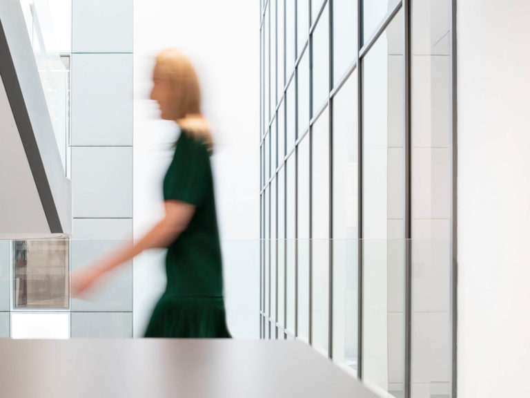 This photograph shows a person in in an office environment. The person is blurred to suggest motion. The person could be a member of the Fintech team.